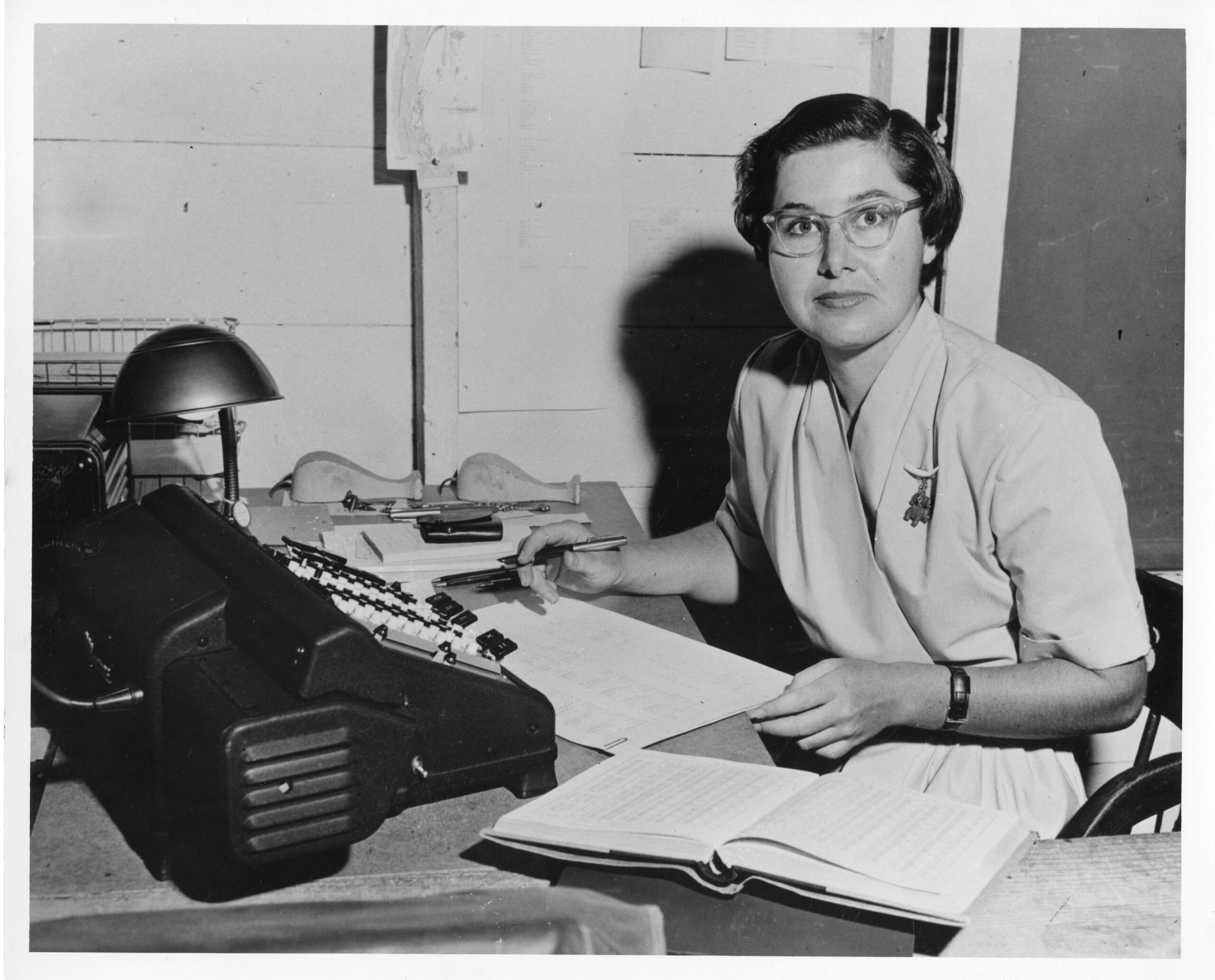 Photo of a woman with a typewriter, open book and pen in hand